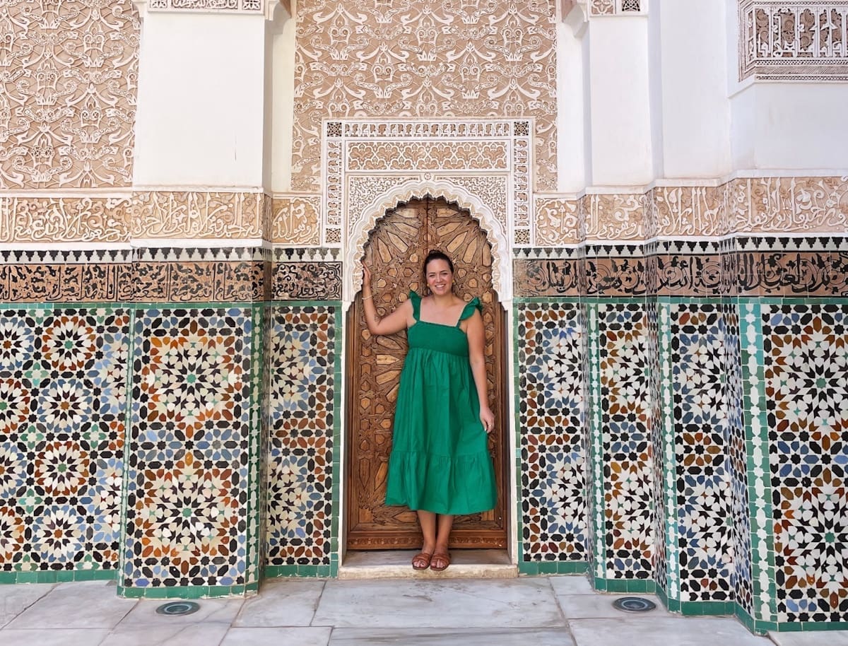 Woman in Green dress standing in front of door surrounded by Moroccan tiles